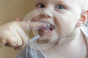 Mom brushes baby`s teeth with a brush that fits on her finger