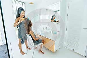 Mom brushing hair to her daughter in hotel bathroom