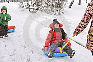 Mom carries a little girl on a sled. behind a boy with a tubing