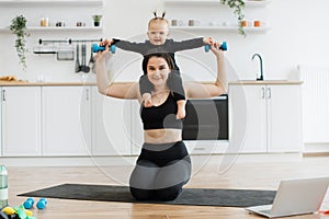 Mom carrying baby with dumbbells on shoulders while sitting
