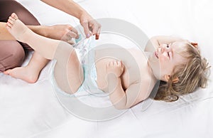 Mom changing diaper to the baby lying on his back