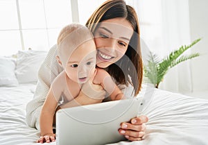 Mom with a child on the bed playing with a tablet, technology