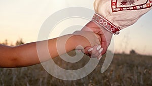 Mom and child holding hands together on wheat field sunset background. Son takes mother hand. Family, trust, love and