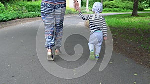 Mom and child holding hands walking together on asphalt road. Gimbal follow
