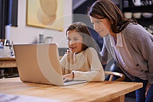 Mom, child and learning with laptop for support, care or browsing in the kitchen at home. Mother, daughter or kid typing