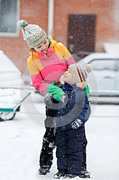 Mom with child playing outdoors at street in winter during snowfall.