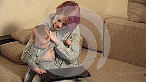 Mom and child are sit and woman working on a laptop baby interferes and closes the gadget a hand