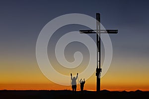Mom with child on top of the mountain near the cross raise their arms in victory photo