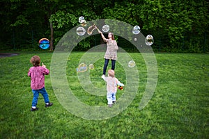 Mom and children playing soap bubbles on the green lawn in the park.