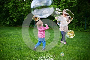 Mom and children playing soap bubbles on the green lawn in the park