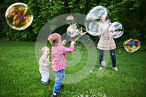 Mom and children playing soap bubbles on the green lawn in the park