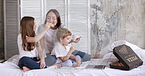 Mom and children on self-isolation eat pizza and watch cartoons on a laptop