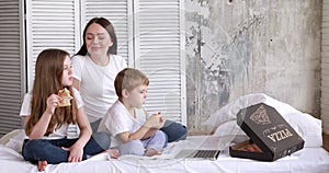 Mom and children on self-isolation eat pizza and watch cartoons on a laptop