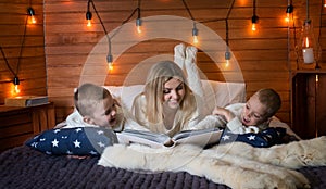 Mom with children in the winter frosty evening sitting on the bed and reading a book together.