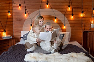 Mom with children in the winter frosty evening sitting on the bed and reading a book together.