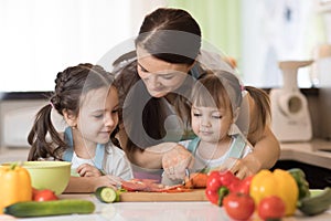 Mom chopping vegetables with kids daughters in a family home kitchen.