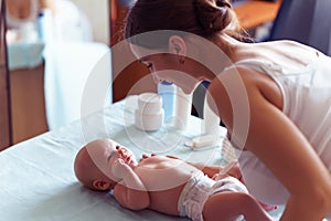 Mom with cute smile takes care of her newborn boy on baby changing table