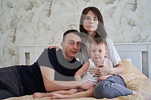 mom dad and baby sit on the bed at home
