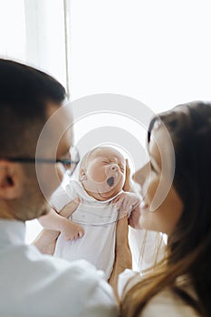 Mom and dad from behind holding their newborn son yawning. New parents