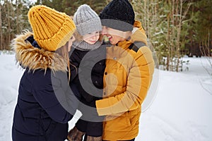 Mom and dad are cuddling and kissing their little son in winter park.