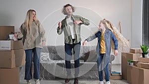 mom dad and daughter are having fun dancing together on moving day, young family surrounded by cardboard boxes