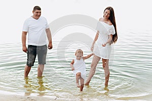 Mom, dad and daughter having fun near lake. The concept of summer holiday. Mother`s, father`s, baby`s day. Family spending time