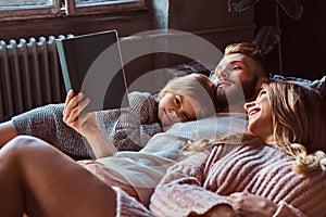 Mom, dad and daughter reading storybook together while lying on bed.