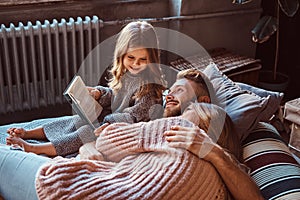 Mom, dad and daughter reading storybook together while lying on bed.