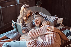 Mom, dad and daughter reading storybook together while lying on bed.