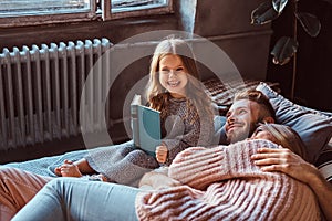 Mom, dad and daughter reading storybook together while lying on bed.