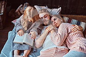 Mom, dad and daughter reading storybook together while lying on bed.