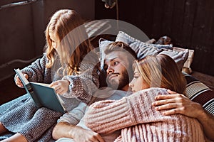 Mom, dad and daughter reading storybook together while lying on bed.