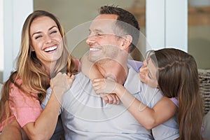 Mom, dad and girl on sofa with smile, embrace and relax in playful bonding together in family home. Mother, father and