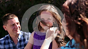 Mom and dad and her little daughter in a park, mom corrects her daughter`s hair.