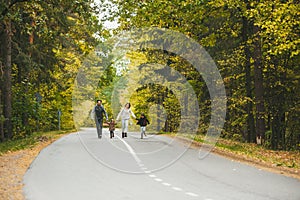 Mom, dad and little childrens, walking on country road. They are talking and enjoying beautiful autumn day