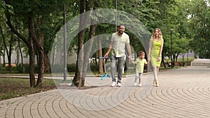 Mom with dad and little son walk in the Park in summer with children`s scooter.