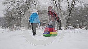 Mom and Dad sledding with a child in the winter forest. parents play a little daughter in a Christmas park. Family plays