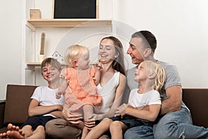 Mom dad and three children are sitting together on couch. Big friendly family