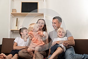 Mom dad and three children are sitting together on couch. Big friendly family