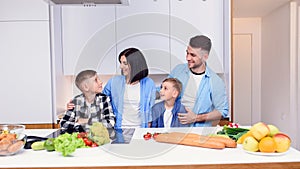 Mom, dad and two sons preparing together healthy breakfast with meat and vegetables on cozy kitchen at dining table.