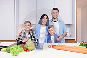 Mom, dad and two sons preparing together healthy breakfast with meat and vegetables on cozy kitchen at dining table.