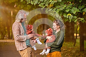 Mom and dad walk in autumn park with twin babies, hold babies in their arms