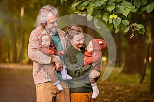 Mom and dad walk in autumn park with twin babies, hold babies in their arms