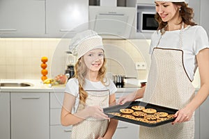 Mom and daughter in aprons and chef hats posing with cookies