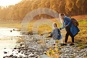 Mom with daughter in autumn. Mother and daughter walking near river in autumn time. Happy family. Fall weekend in the open air. Fa