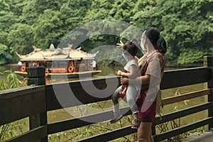 Mom and daughter in baby carrier watching pleasure boat with mask