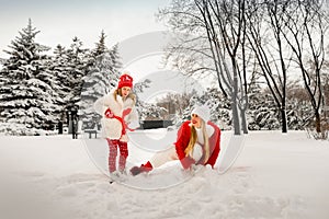 Mom and daughter in beautiful winter clothes play snowballs in a winter park