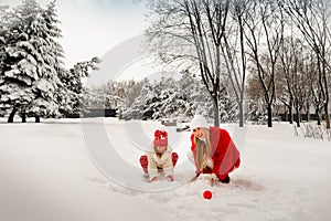 Mom and daughter in beautiful winter clothes play snowballs in a winter park