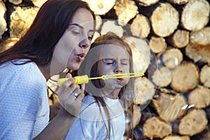 Mom and daughter blow bubbles on the background of firewood. Happy woman with child blow bubbles near stacked firewood.