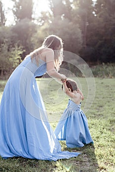 Mom with daughter in blue long indentical dresses on grass in forest